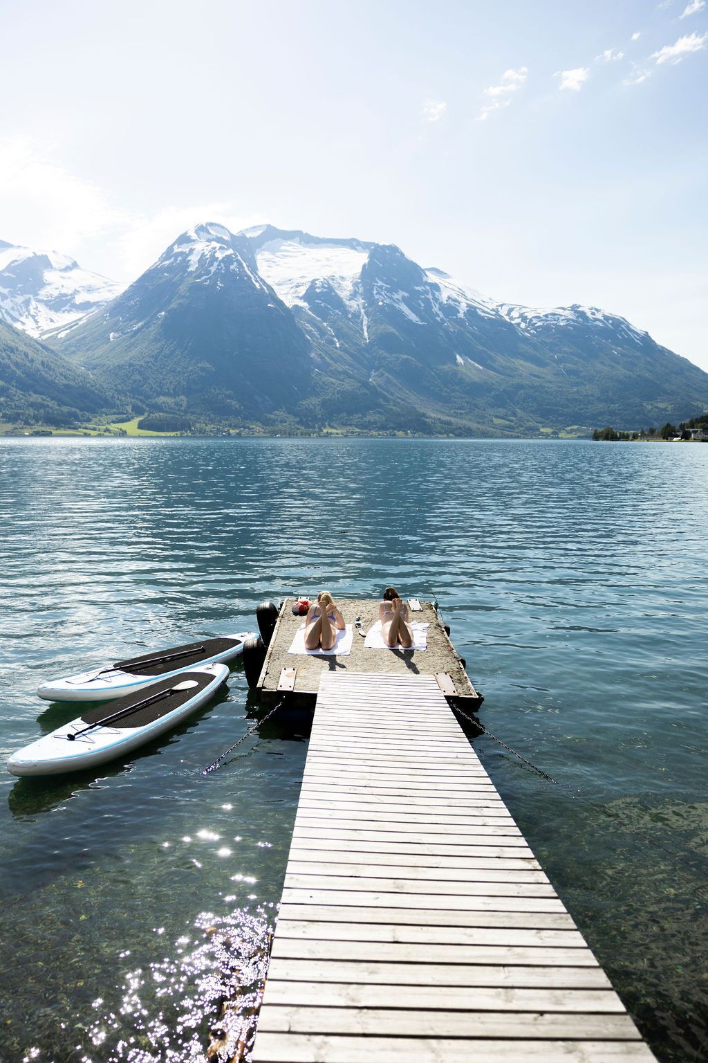 A wooden dock extending into a lake with two paddleboards and two people sitting on the dock.