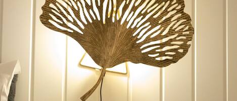 Una habitación con una mesita de noche blanca, un florero de vidrio transparente con flores blancas y un adorno en la pared.