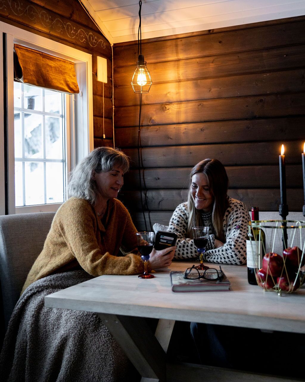 Twee personen zitten aan een tafel met een kaars, een wijnglas en een boek.