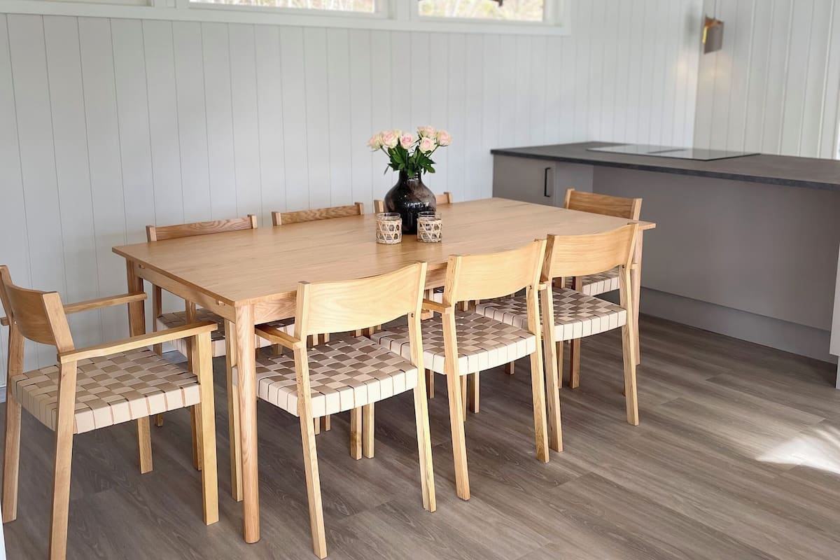 Un comedor con una mesa y sillas de madera, un jarrón con flores e iluminación colgante.