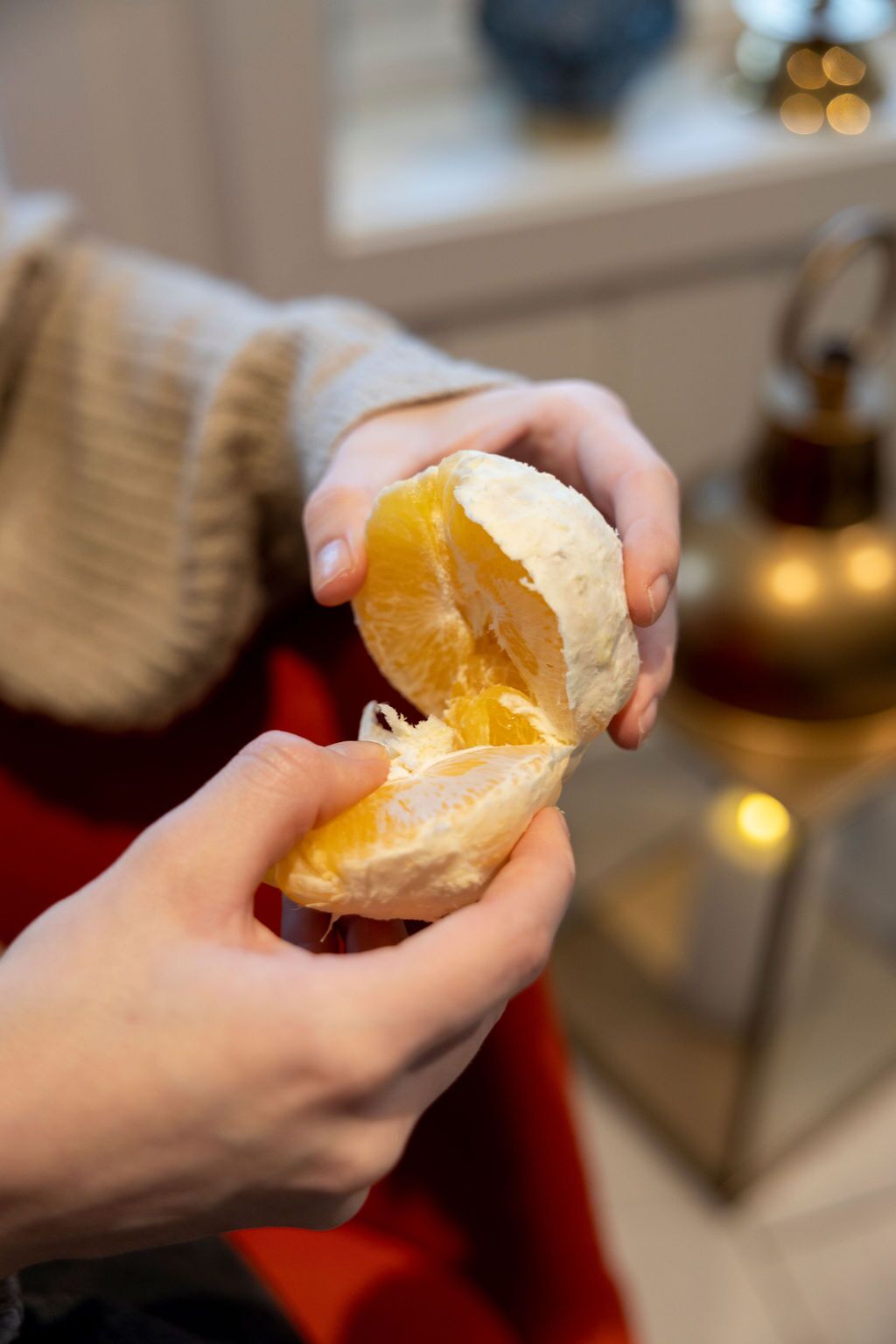 A person holding an orange, with a blurred background including a window and a decorative item.