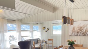 A modern dining area with a wooden table and chairs, a vase of flowers, and a view of mountains through large windows.
