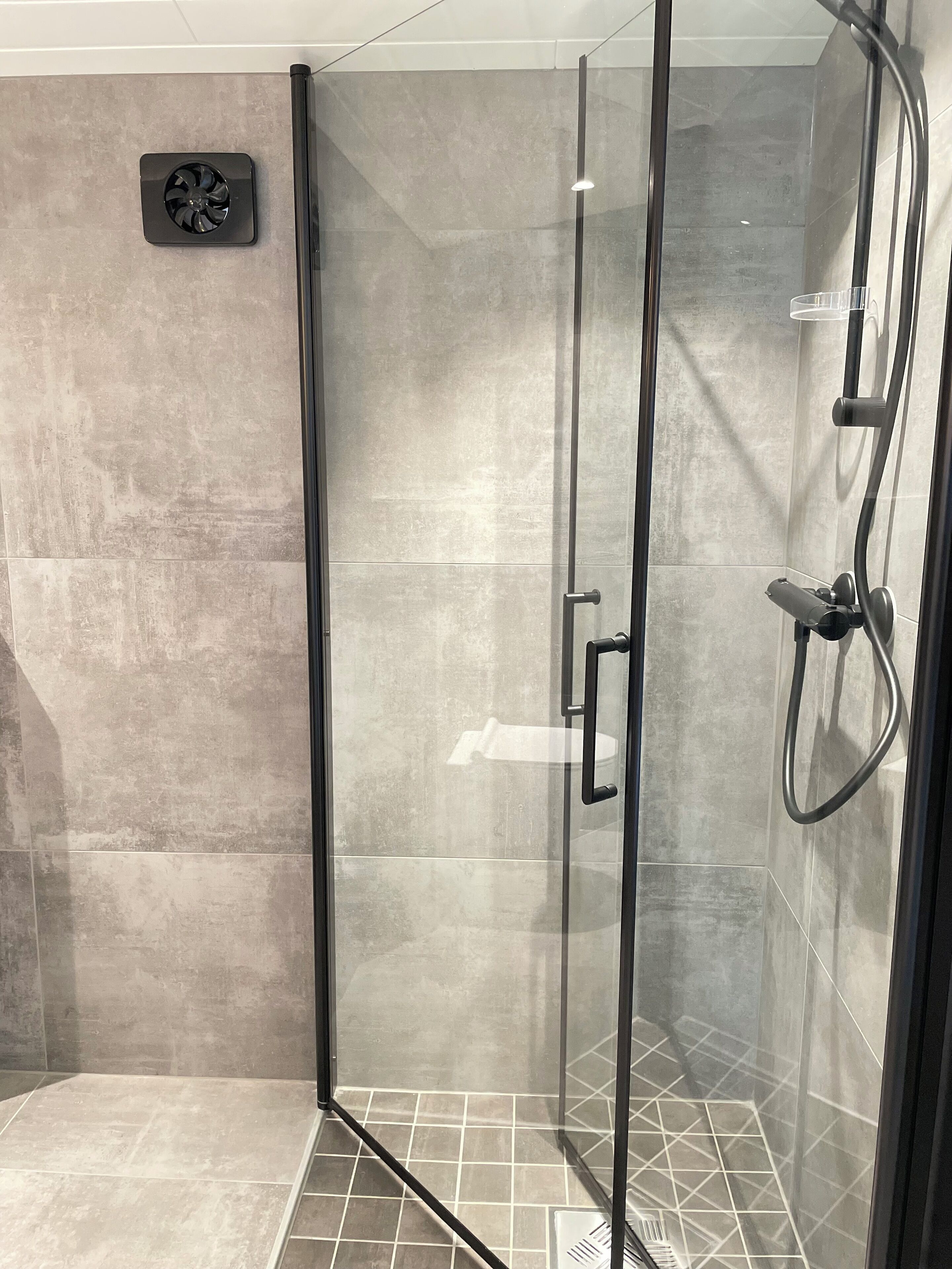 A modern shower with a glass door, a handheld showerhead, and a wall-mounted fan.