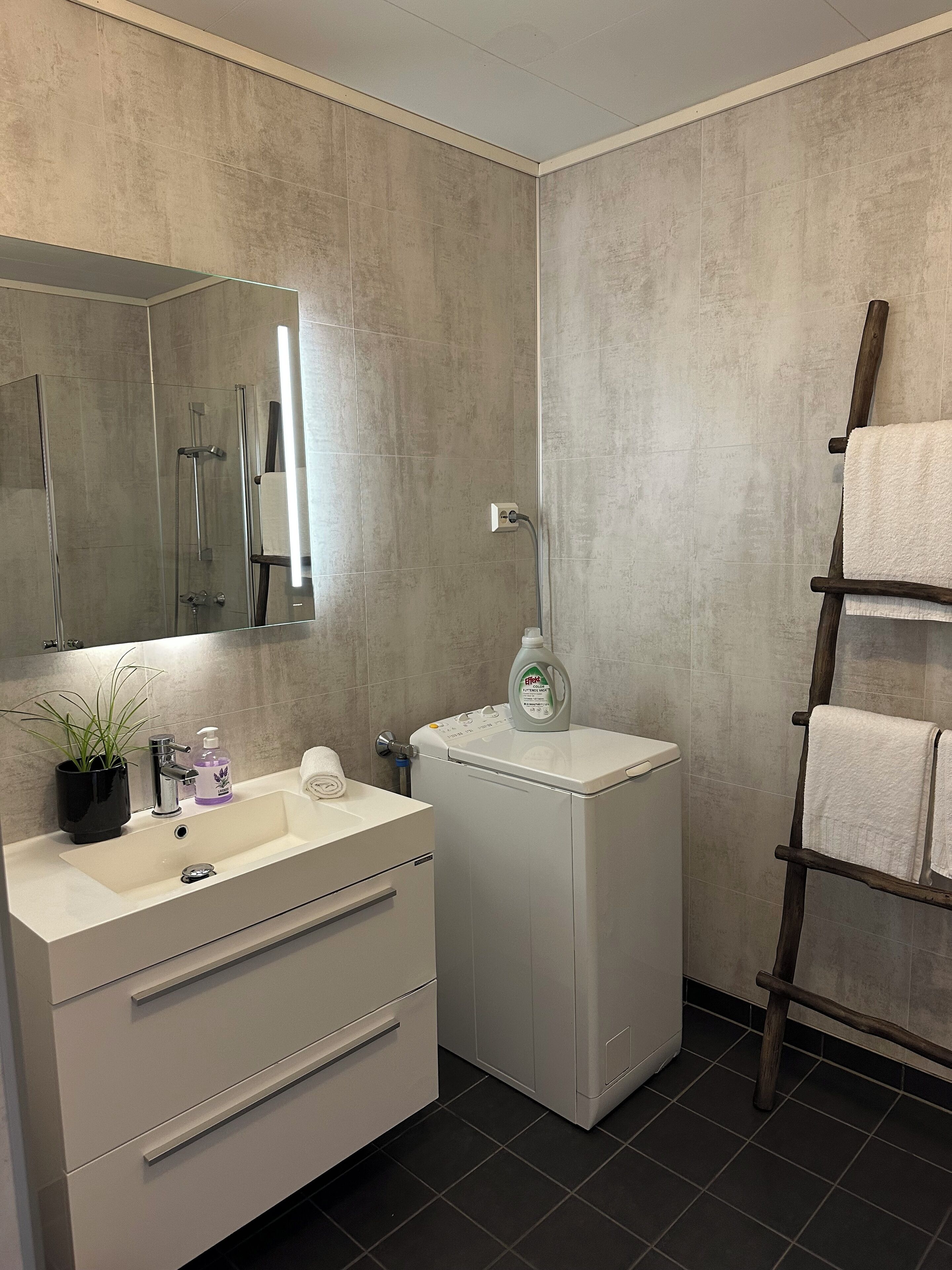 Ein modernes Badezimmer mit einem großen Spiegel, einem Waschbecken mit Armatur, einem Handtuchhalter und einer Waschmaschine.