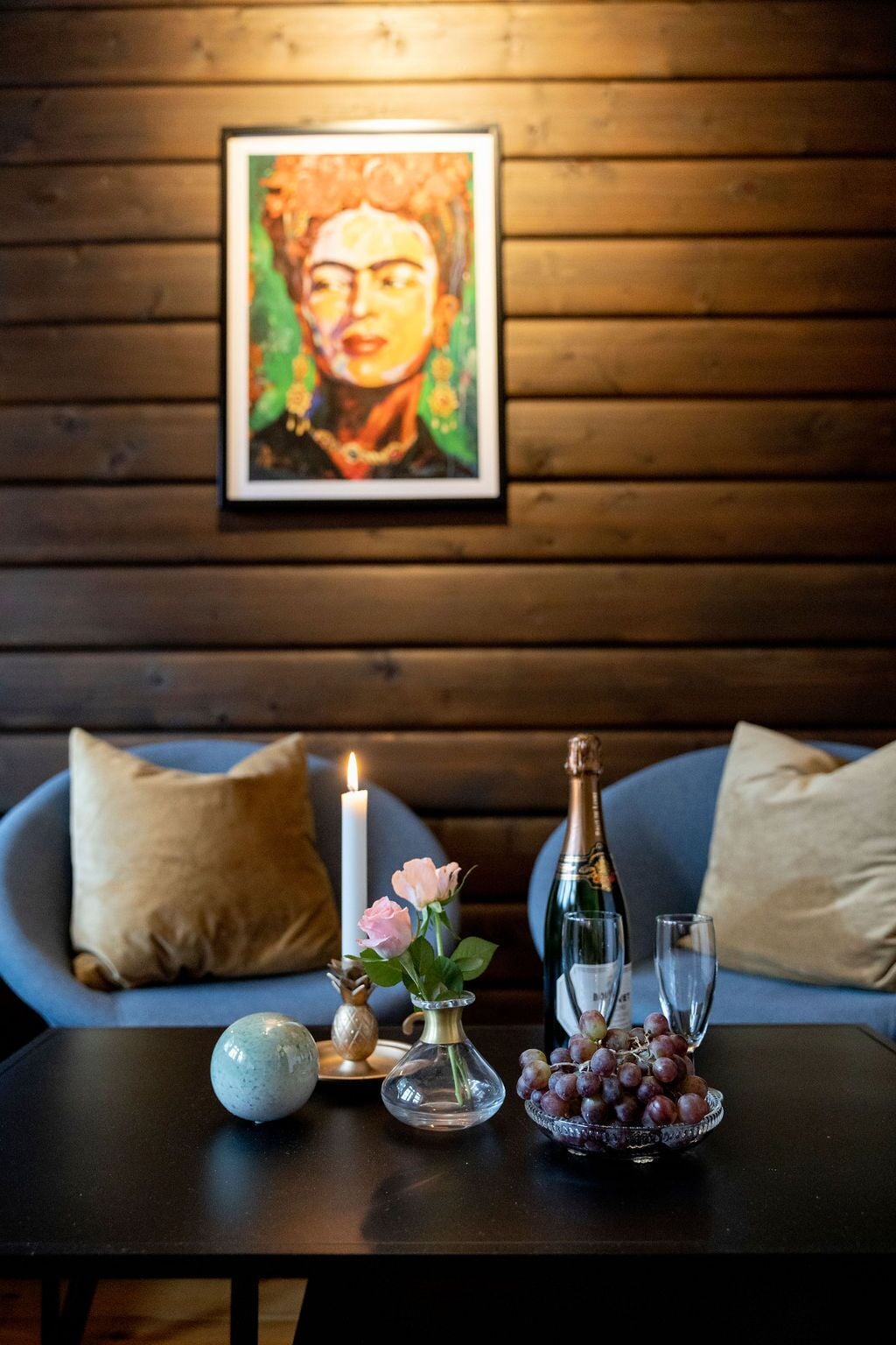 Une table avec une bougie, une bouteille de champagne, des verres, un vase rempli de fleurs et un bol de raisins.