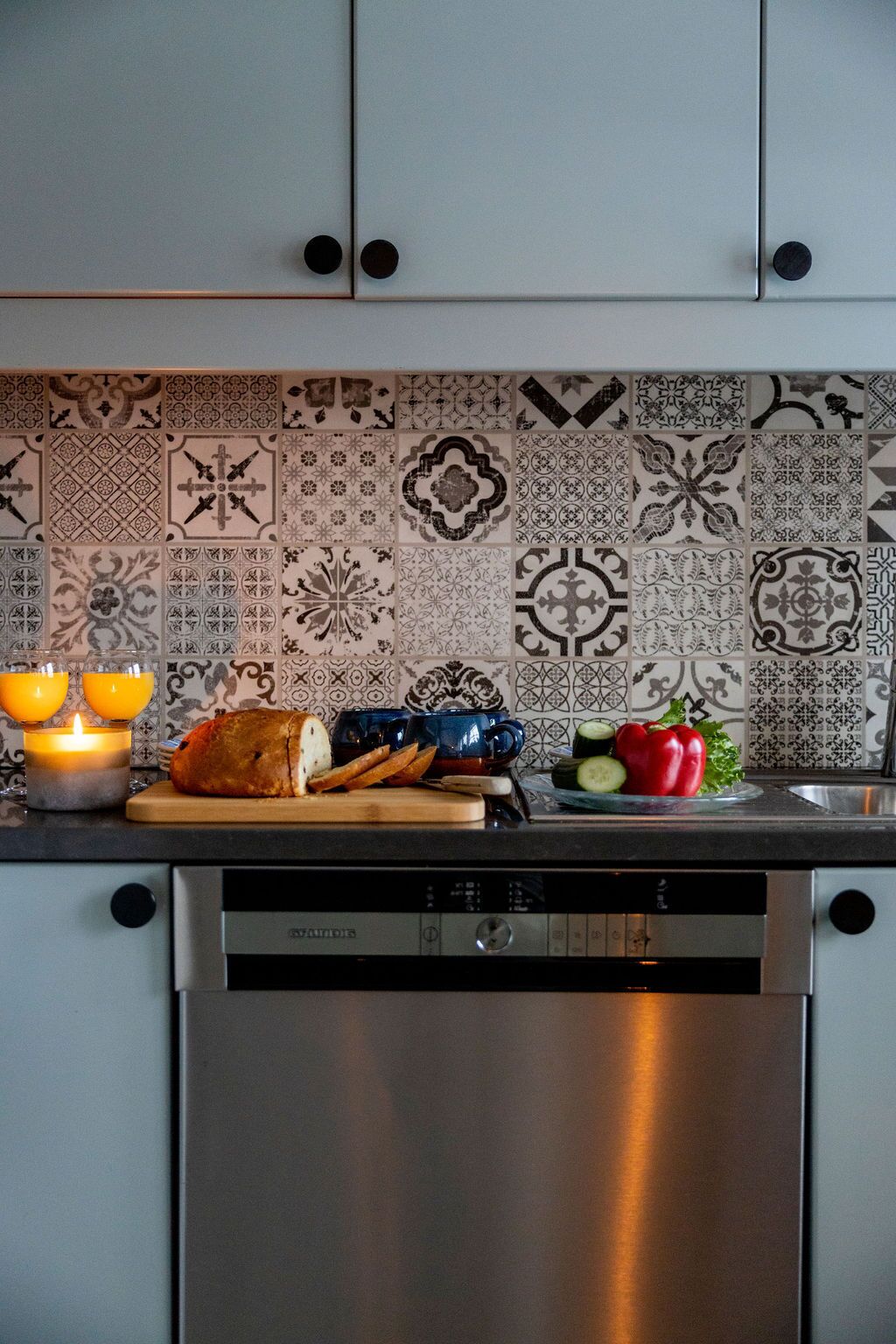 Et køkken med tapetseret backsplash, et brød, et skærebræt, en blå kop, en rød peberfrugt og et lys.