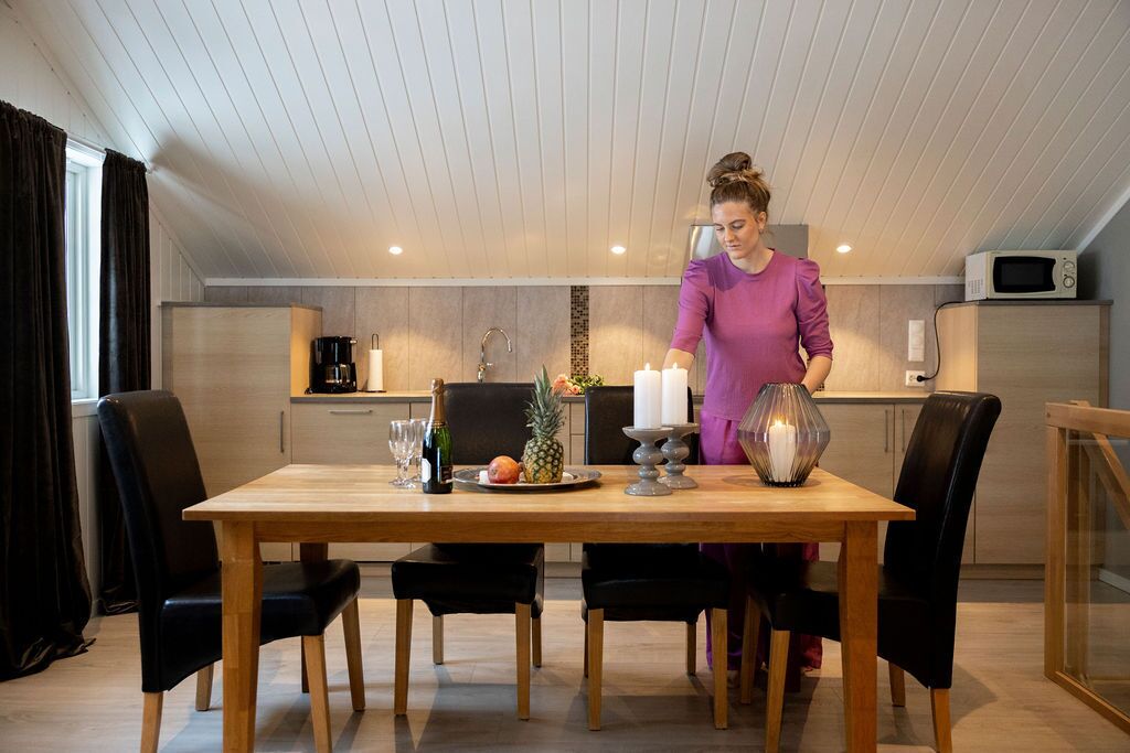 A modern kitchen with a wooden dining table, black chairs, and a person standing by the counter.