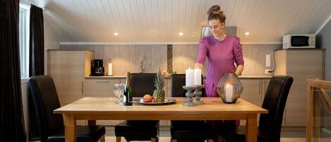 A modern kitchen with a wooden dining table, black chairs, and a person standing by the counter.