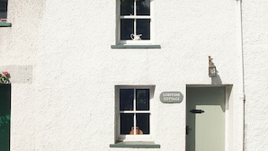 A white building with a sign reading 'LOBSTONE COTTAGE,' a door, and a window with a heart-shaped decoration.