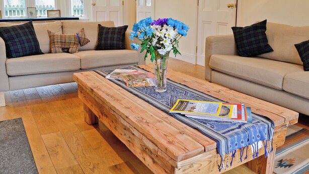 Ein Wohnzimmer mit zwei beigen Sofas, einem Holztisch mit Zeitschriften und einer Blumenvase.