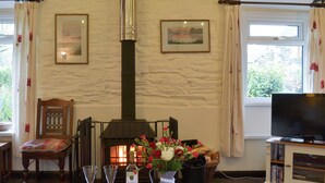 A cozy living room with a fireplace, a television, and a dining area with a table set for two. - Trenay Barns Cottage (St Neot, near Liskeard)