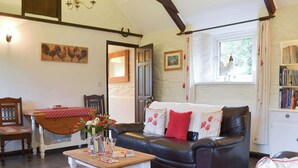 A cozy living room with a leather sofa, a wooden coffee table with drinks, a patterned rug, and a bookshelf filled with books. - Trenay Barns Cottage (St Neot, near Liskeard)