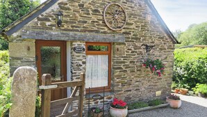 A stone cottage with a wooden door, a welcome sign, a wheel, and potted plants. - Trenay Barns Cottage (St Neot, near Liskeard)