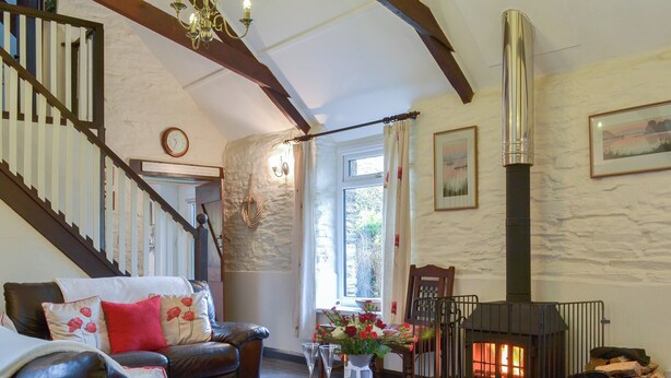 A cozy living room with a fireplace, leather sofa, and a staircase. - Trenay Barns Cottage (St Neot, near Liskeard)