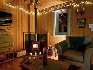 A cozy room with a fireplace, wooden walls, a sofa, and a table with a bottle and glass. - 2 bedroom accommodation in Uplowman, near Tiverton (Uplowman, near Tiverton)