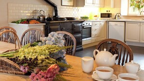 A kitchen with white cabinets, a stove, and a dining table set with flowers and teacups. - 5 bedroom accommodation in Kildale, near Whitby (Kildale, near Whitby)