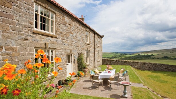 A stone building with a patio table and chairs, surrounded by a stone wall and a grassy field. - 5 bedroom accommodation in Kildale, near Whitby (Kildale, near Whitby)