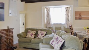 A living room with a sofa set, a fireplace, a dining table with chairs, and a window with curtains. - Rockville Cottage - 24376 (Bempton, near Flamborough)