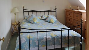 A bedroom with a bed, a nightstand, a lamp, a dresser, and a wall-mounted light fixture. - Rockville Cottage - 24376 (Bempton, near Flamborough)
