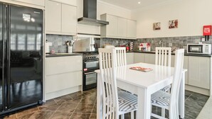 A modern kitchen with white cabinetry, a black refrigerator, a stove, and a microwave. There are two white chairs around a table. - 1 bedroom accommodation in Broadstairs (Broadstairs)