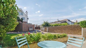 A patio with two blue chairs and a table, surrounded by a brick wall and greenery. - 1 bedroom accommodation in Broadstairs (Broadstairs)