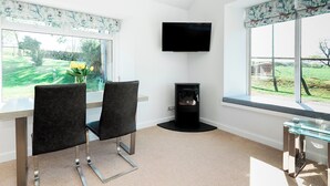 A modern living room with a flat-screen TV mounted on the wall, two black chairs with metal legs, a glass coffee table, and a fireplace.