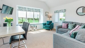 A modern living room with a dining area, large windows, and a flat-screen TV.