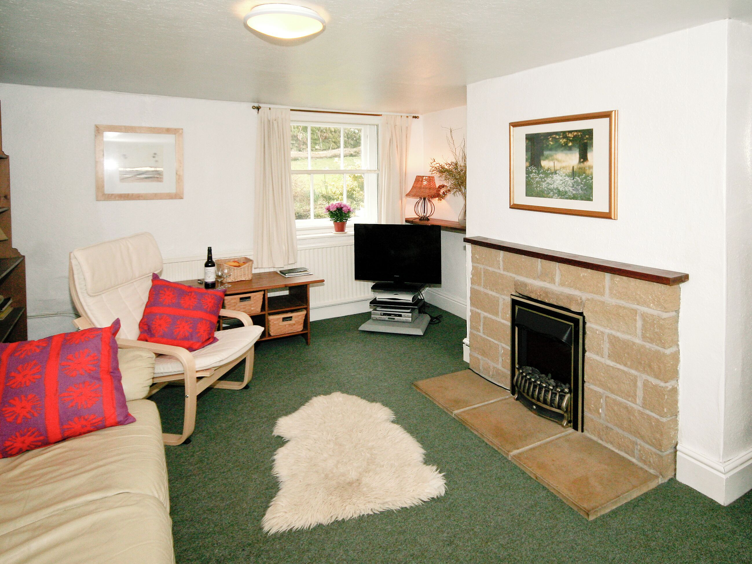 A living room with a fireplace, a television, a sofa, and a window with curtains.