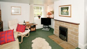 A living room with a fireplace, a television, a sofa, and a window with curtains. - Drum And Monkey Cottage (Chapel-en-le-Frith)