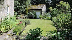 A stone building with a moss-covered roof, surrounded by a well-maintained garden with a variety of plants and a clear lawn. - Drum And Monkey Cottage (Chapel-en-le-Frith)