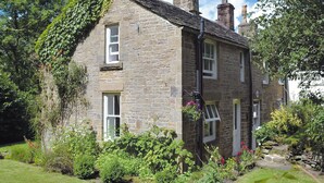 A stone house with a gabled roof, a small front porch, and a garden with various plants and flowers. - Drum And Monkey Cottage (Chapel-en-le-Frith)