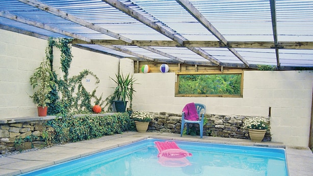 A covered swimming pool with a stone wall, potted plants, and a blue chair. - Drum And Monkey Cottage (Chapel-en-le-Frith)