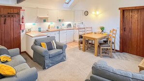 A modern kitchen with white cabinets, a dining table with chairs, and a gray sofa with yellow cushions. - 2 bedroom accommodation in Shipton Gorge (Shipton Gorge)