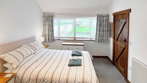 A bedroom with a large bed, a wooden wardrobe, a window with curtains, and a small table. - 2 bedroom accommodation in Shipton Gorge (Shipton Gorge)