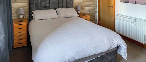 A bedroom with a large bed, wooden headboard, two bedside tables with lamps, a wooden door, and a poster on the wall.