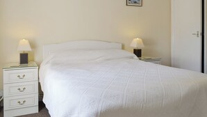 Een net opgemaakt bed met een witte deken en twee bedlampen op witte nachtkastjes. Boven het bed hangen twee ingelijste foto's.