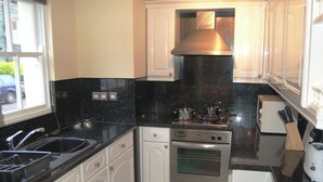 A compact kitchen with white cabinets, a black countertop, a stainless steel stove, and a microwave. - Helvellyn House Apartment (Keswick)
