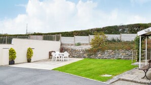 A backyard with a lawn, a white table and chairs, a stone wall, and a wooden fence.
