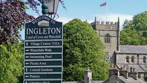 A signpost with directions to various attractions in Ingleton, including the Village Centre, Waterfalls Walk, Swimming Pool, Picnic Area, Central Gardens, Pottery, and Climbing Wall.
