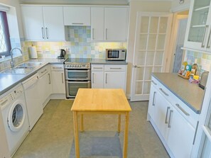A compact kitchen with white cabinets, a microwave, an oven, a washing machine, and a wooden table.