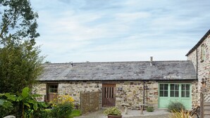 A stone cottage with a gravel driveway, a wooden door, and a green window. - Penno Cottage - 24440 (Bodmin)