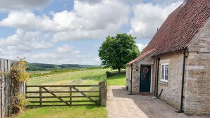 A stone building with a tiled roof, a wooden gate, and a grassy field in the background. - Moorhouse Farm Cottage (Hovingham, near York)