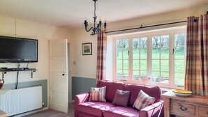 A cozy living room with a red sofa, a television, a wooden desk, and a window with curtains. - Moorhouse Farm Cottage (Hovingham, near York)