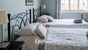 A bedroom with two beds, a bedside table, a lamp, a window with curtains, and a framed picture on the wall. - Moorhouse Farm Cottage (Hovingham, near York)