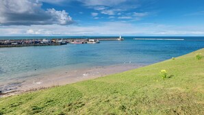 A coastal view with a grassy area, a dock with boats, and a lighthouse in the distance. - 2 bedroom accommodation in Seahouses (Seahouses)