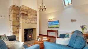 A living room with a stone fireplace, blue sofas, a wooden coffee table, and a painting on the wall. - 2 bedroom accommodation in Seahouses (Seahouses)