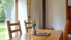 Une table à manger en bois, des chaises, un vase rempli de fleurs et une bouteille de vin.