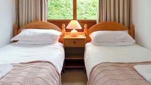 Une chambre avec deux lits simples, une table de chevet avec une lampe et une fenêtre avec des rideaux.