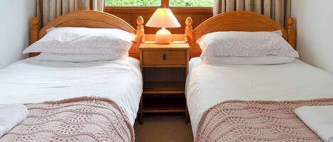 A room with two single beds, a nightstand with a lamp, and a window with curtains.