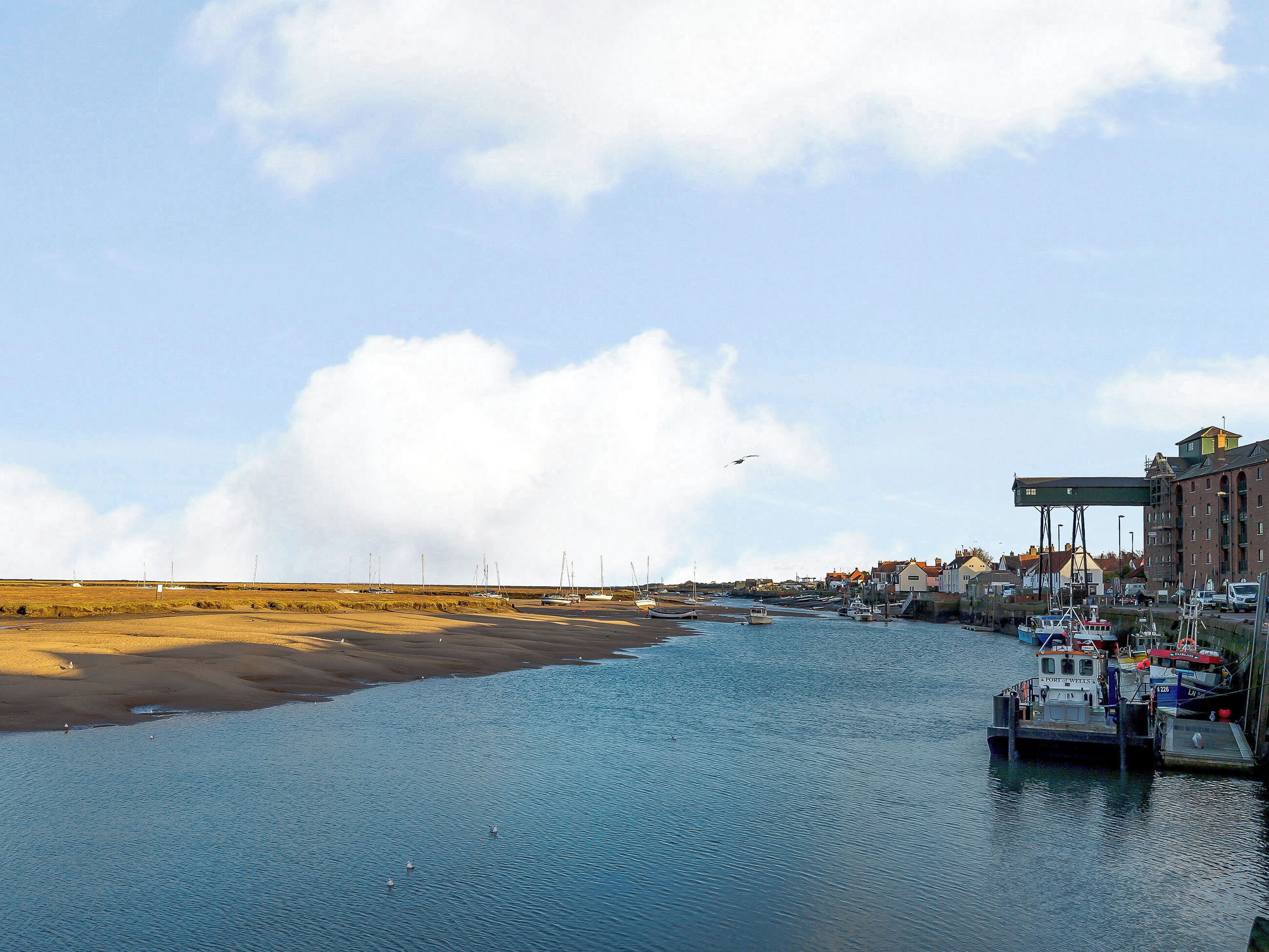 A river with boats docked on the right, a bridge, and buildings along the riverbank.